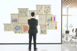 A man in suit analyzes colorful charts and sketches on a wall in a modern office setting.