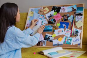 A person adds images and notes to a colorful corkboard filled with travel inspirations, motivational quotes, and memories.