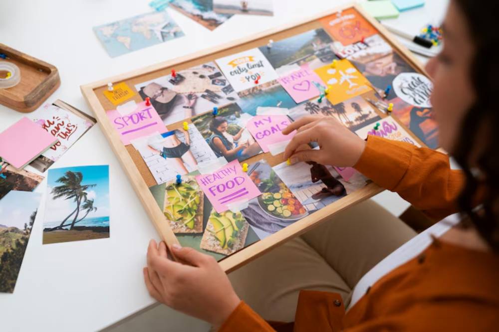 A person arranges a vision board with photos and sticky notes labeled 'Sport,' 'Healthy Food,' and 'My Goals,' on a white table.