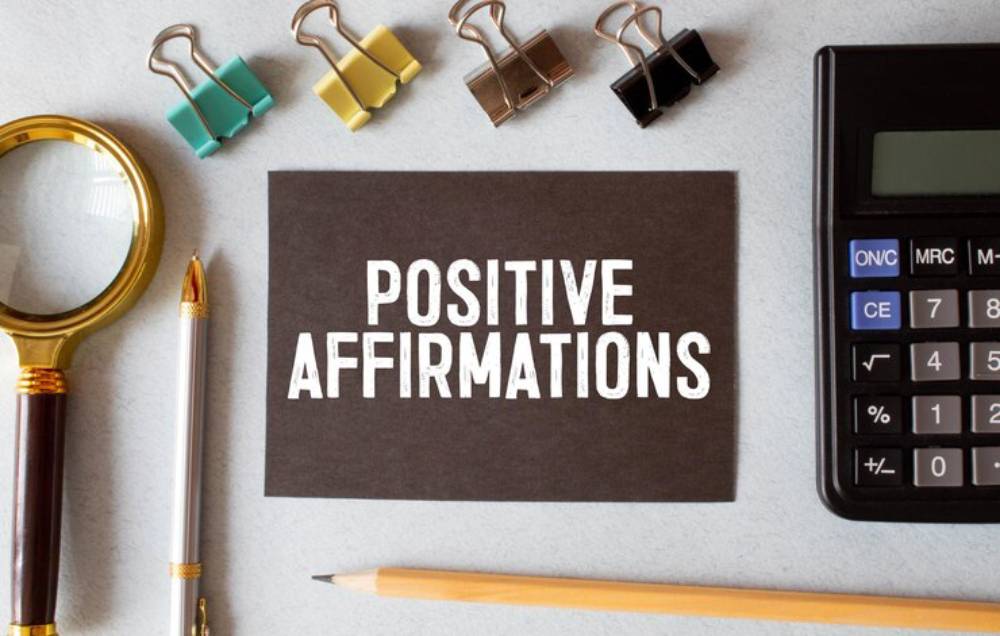 A workspace featuring a card that reads 'Positive Affirmations,' surrounded by stationery items like paper clips, a magnifying glass, and a calculator.