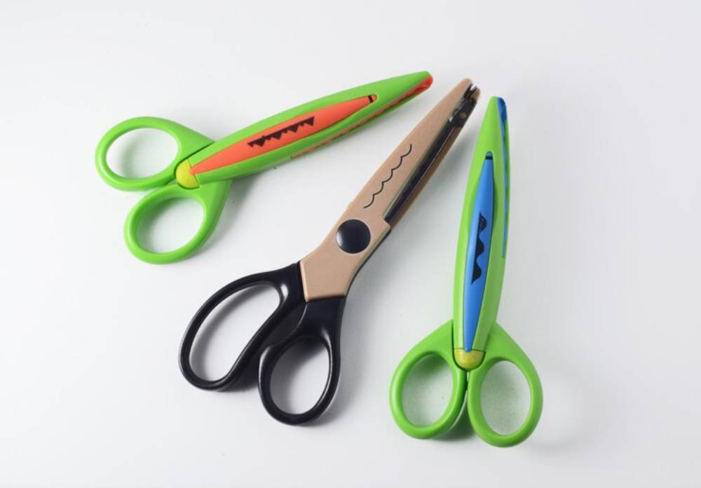 Three pairs of colorful, child-friendly scissors arranged on a white background, featuring playful designs and vibrant colors.