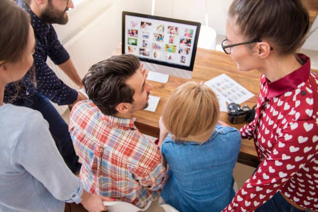 A group of people gathered around a computer, viewing images on the screen for making vision board, with a camera placed on the table.