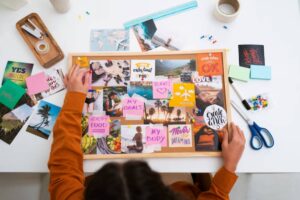 A person arranging a vision board with motivational images and sticky notes about goals, travel, and healthy living on a table.