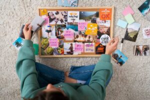 A person arranging a vision board with photos and motivational notes, focusing on goals like travel, health, and self-improvement.
