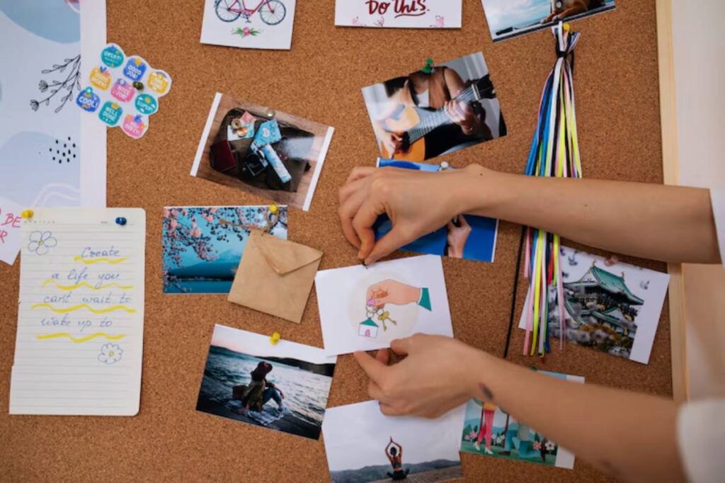 A hand pins a colorful card to a corkboard filled with inspirational photos and notes, reflecting creativity and positivity.